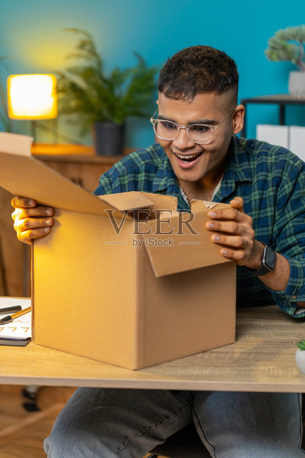 快乐的男士购物者在家中办公室拆开纸箱快递包裹。照片摄影图片