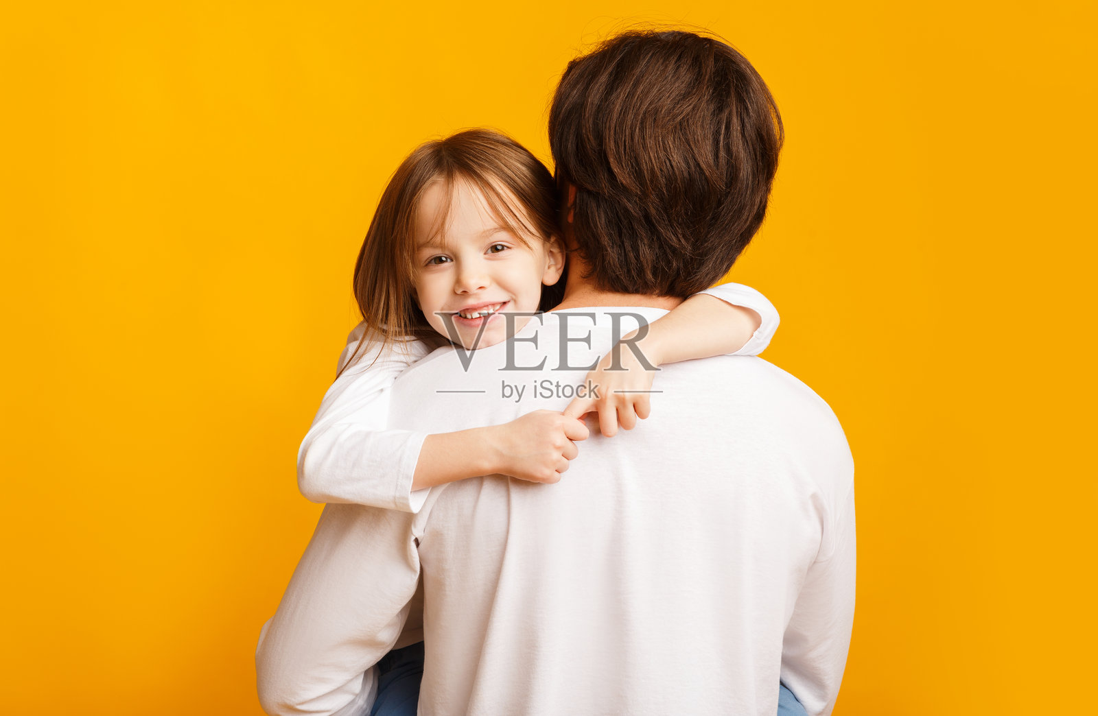 可爱的小女孩在黄色背景下拥抱她的爸爸照片摄影图片