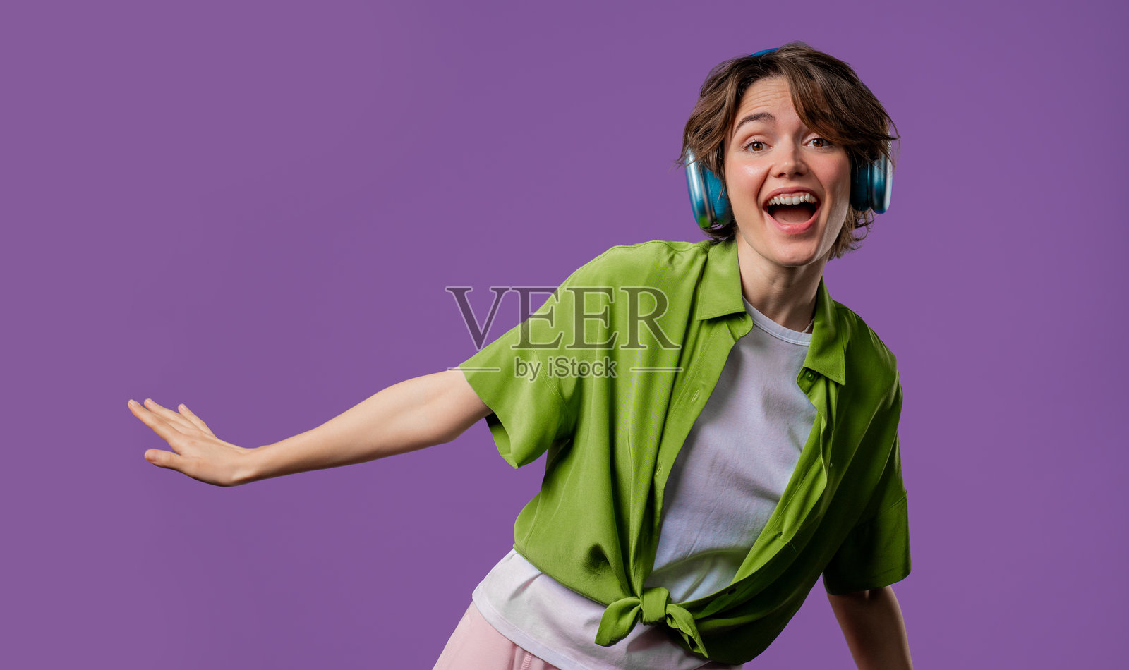 快乐的女人在紫色工作室背景下，戴着耳机享受音乐和舞蹈。无线现代音响技术，在线播放器。照片摄影图片