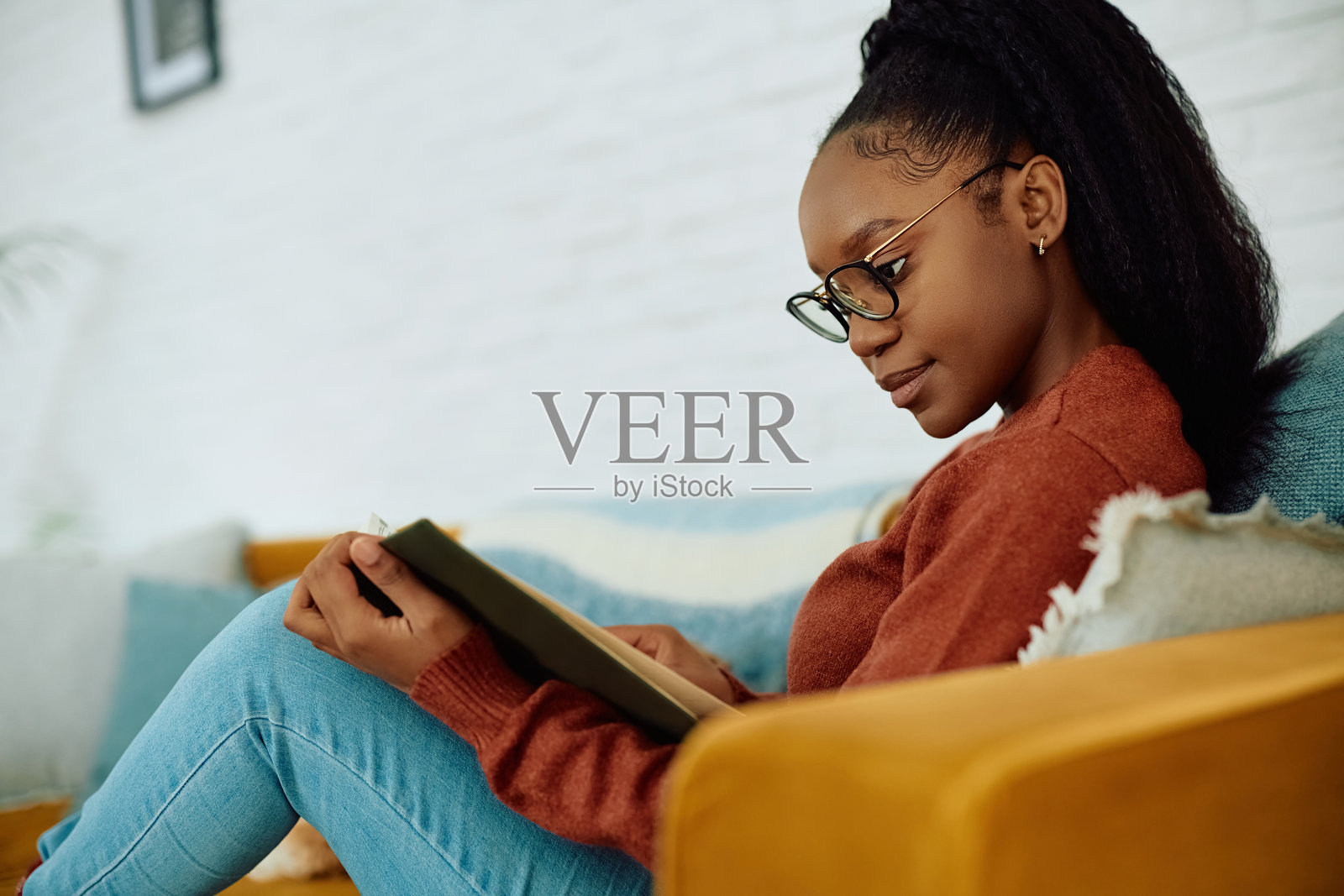 年轻的黑人女性在沙发上放松，阅读一本书。照片摄影图片