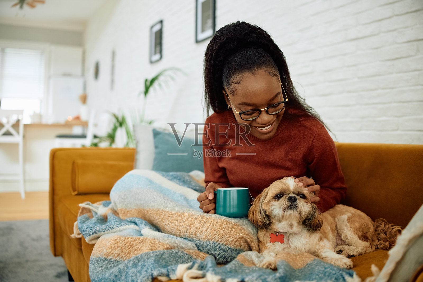 快乐的黑人女性在家中与她的狗一起放松，喝着茶。照片摄影图片