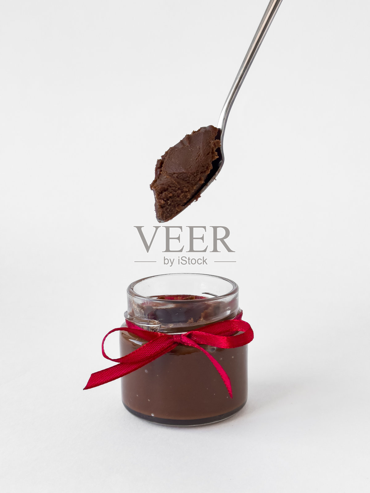 美味的巧克力酱装在玻璃罐中，系着红色丝带，上面有一勺巧克力酱。照片摄影图片