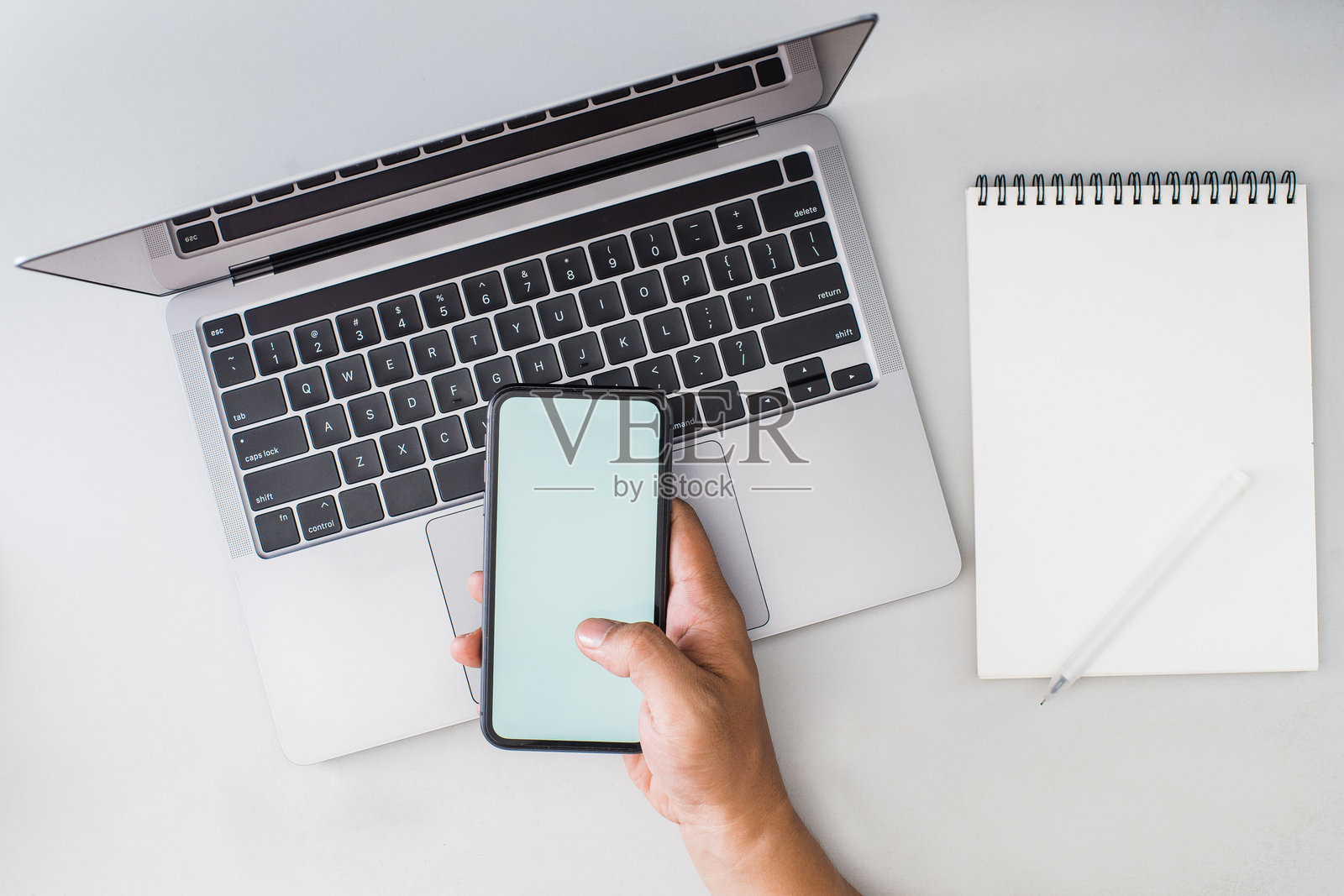 从上方拍摄的图像，显示一个人在笔记本电脑前工作时查看手机。照片摄影图片