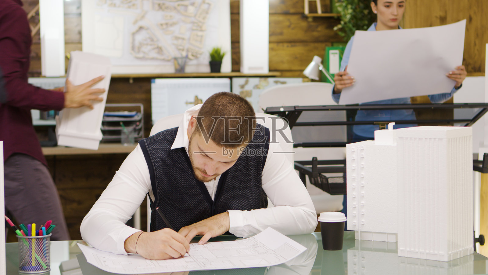 疲惫的年轻建筑师喝着咖啡，正在绘制房屋设计图。照片摄影图片