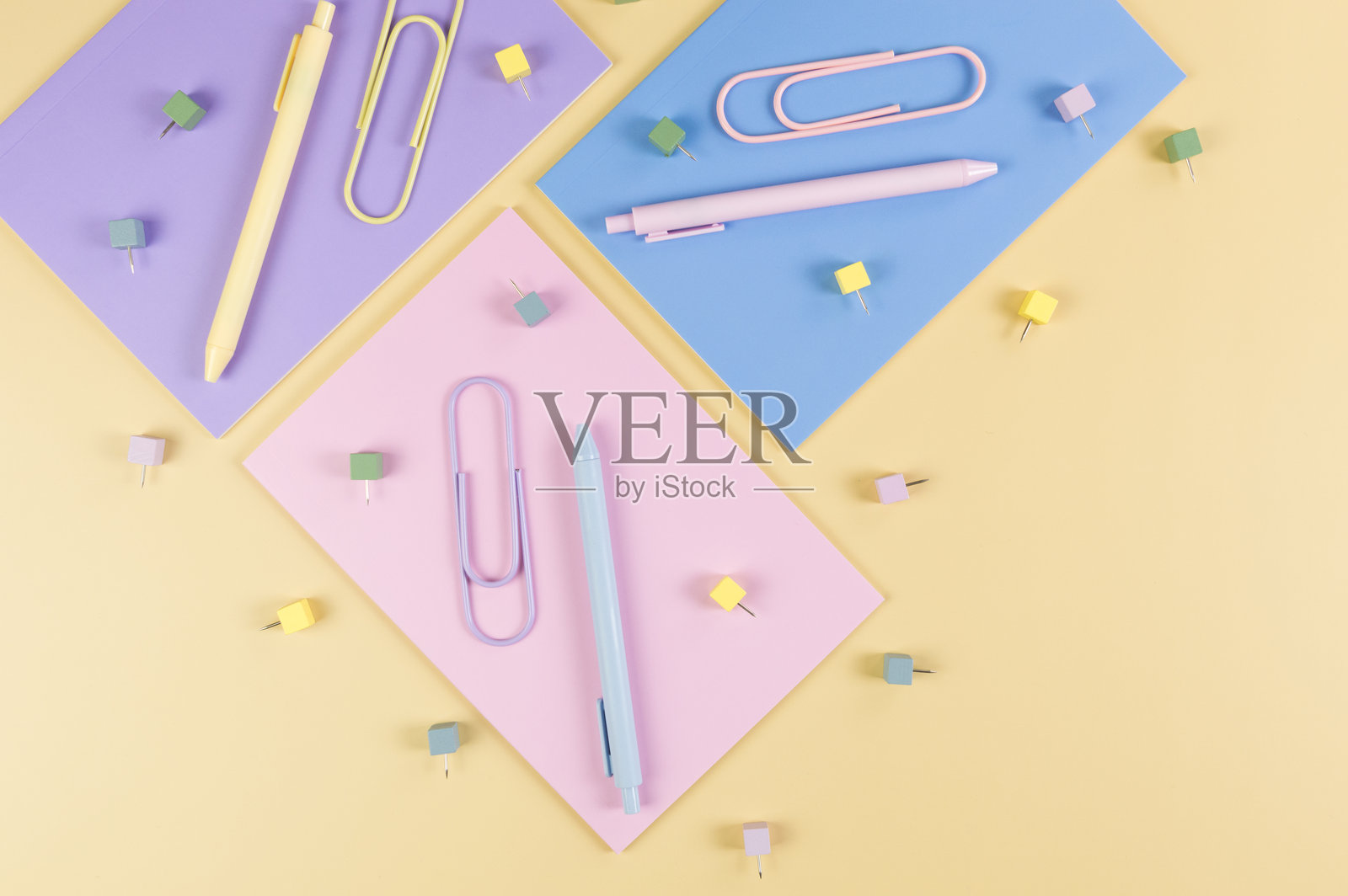 从上方俯视粉色、紫色和蓝色的笔记本，背景为黄色。五彩缤纷的笔、纸夹、图钉，学校和办公室的壁纸。照片摄影图片