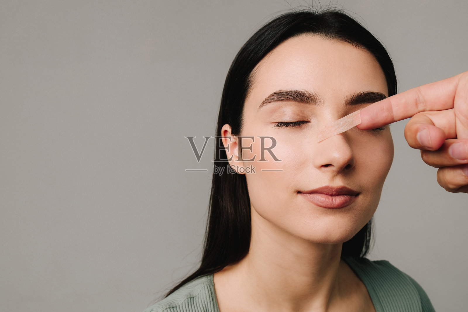 鼻整形手术。整形外科医生在鼻整形恢复期间为患者贴鼻子。手术后在鼻子上贴上绷带，以支持其形状，减少肿胀并改善外观。照片摄影图片