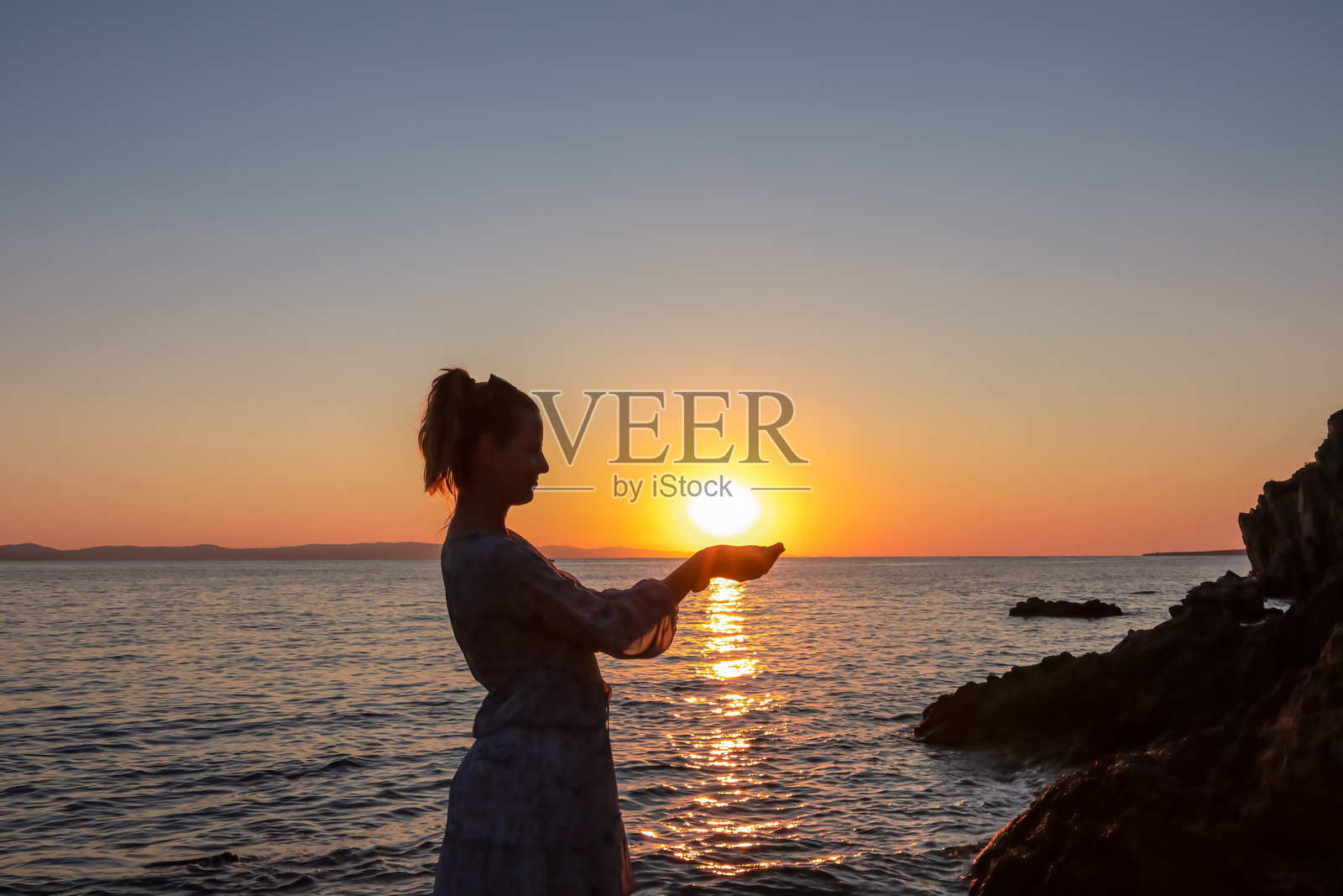 西索尼亚 - 一位游客女性的剪影在卡里迪海滩上举着太阳，俯瞰爱琴海的日落全景照片摄影图片