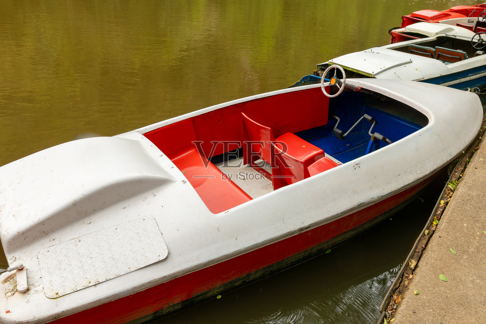一只小红白相间的船停在水中，停靠在码头旁边。照片摄影图片