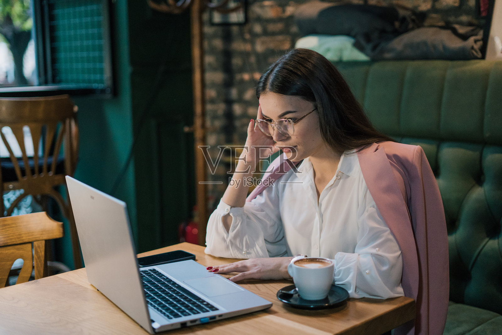 一位迷人的年轻女性在咖啡馆里坐着，手里拿着笔记本电脑和一杯咖啡。照片摄影图片