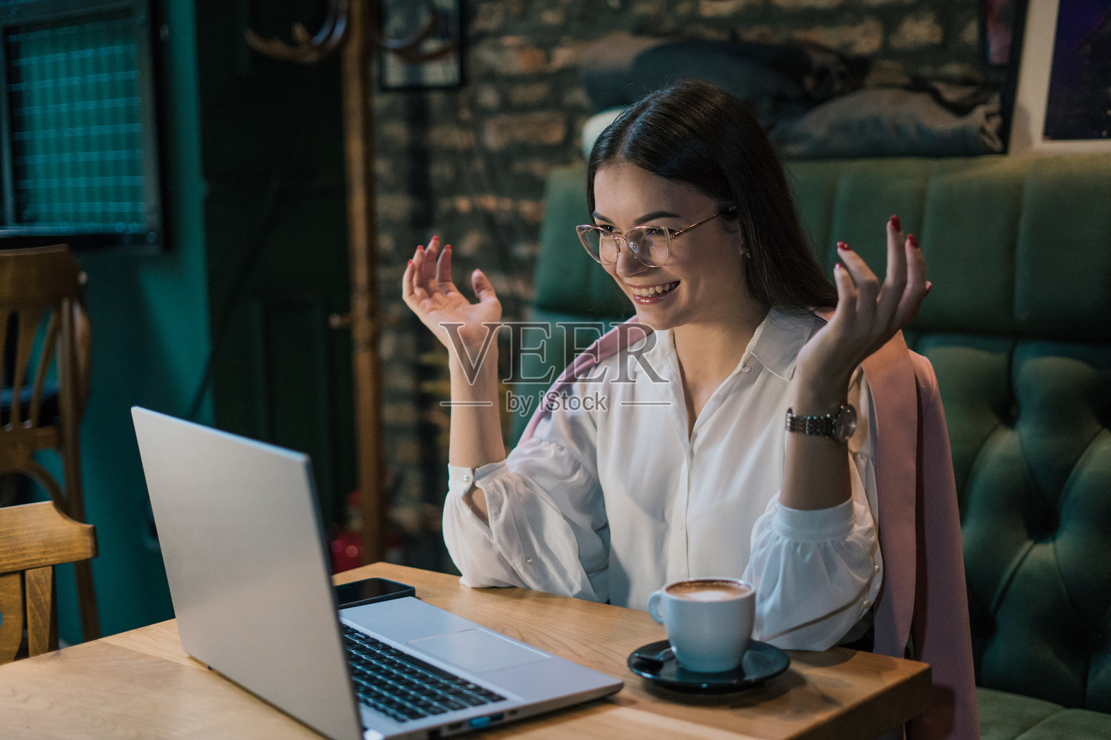 一位迷人的年轻女性在咖啡馆里坐着，手里拿着笔记本电脑和一杯咖啡。照片摄影图片