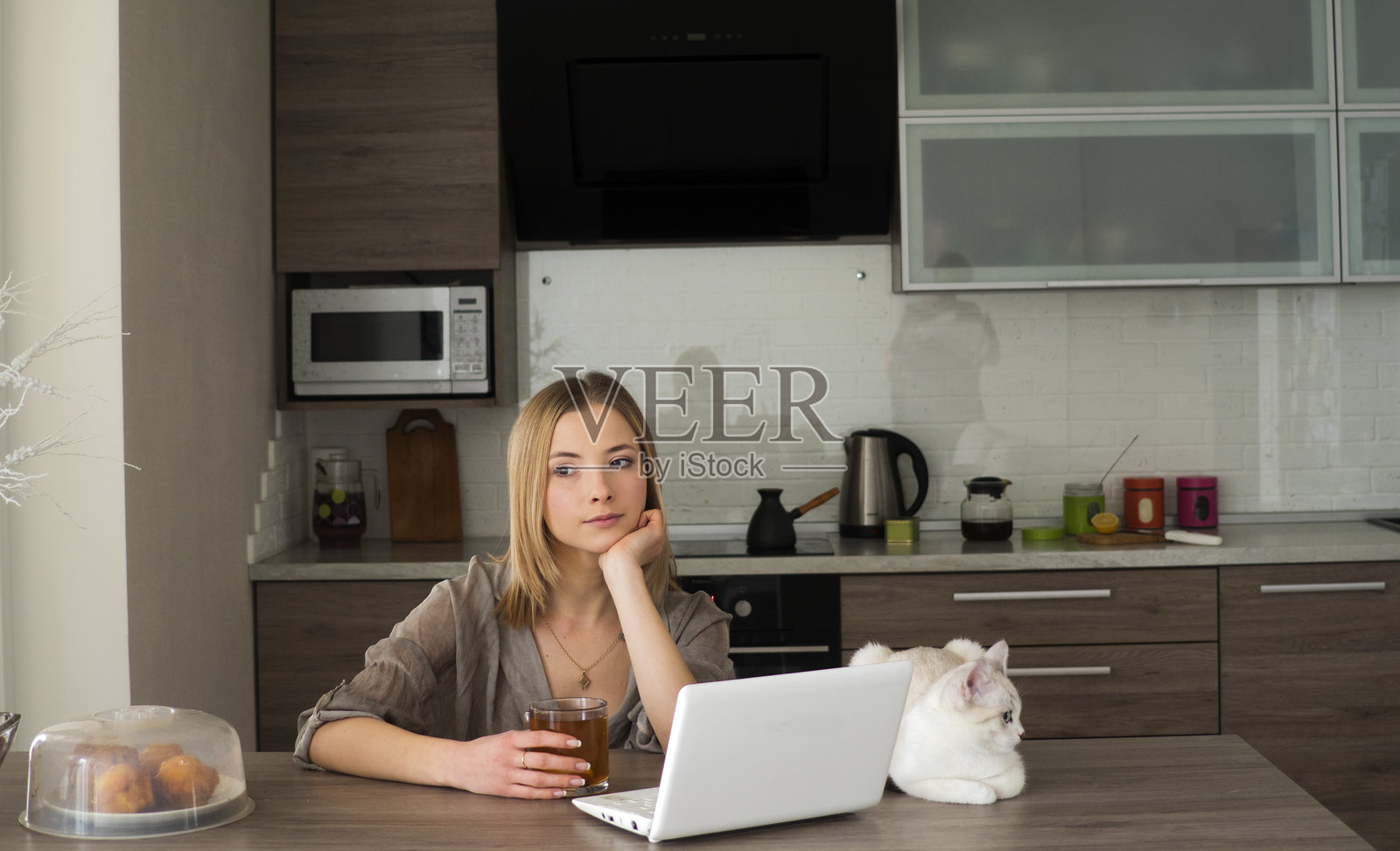 思考中的年轻女性在厨房桌子上使用笔记本电脑，旁边有一只猫。照片摄影图片
