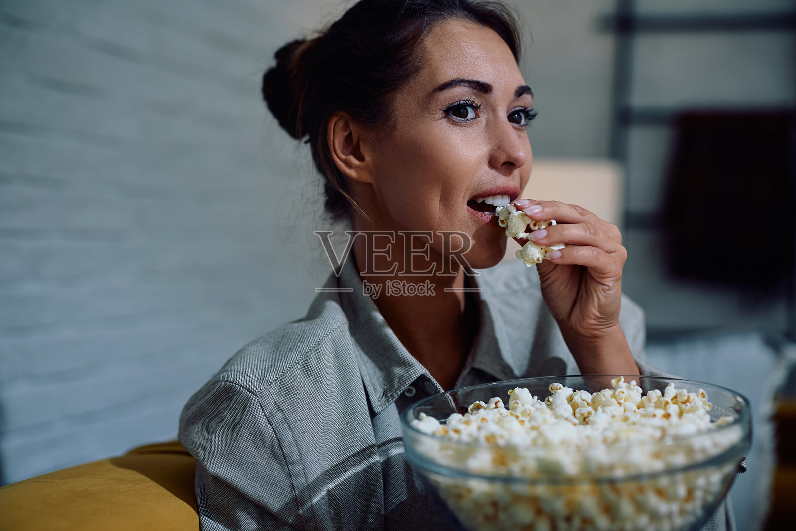 年轻女性在家看电视时吃爆米花。照片摄影图片