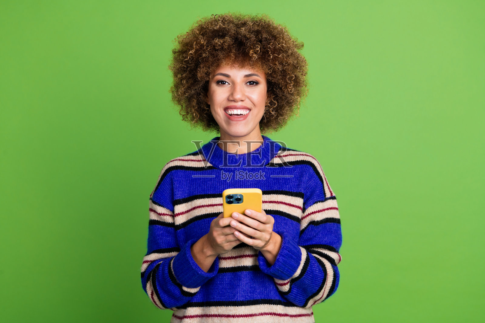 可爱的女性穿着蓝色条纹时尚服装，手持现代设备，背景为绿色。照片摄影图片