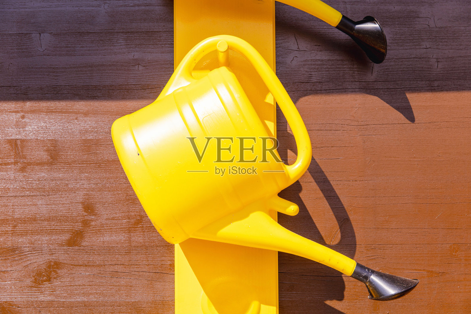 明亮的黄色浇水壶挂在黄色涂漆的木墙上，园艺工具，夏季户外装饰概念照片摄影图片