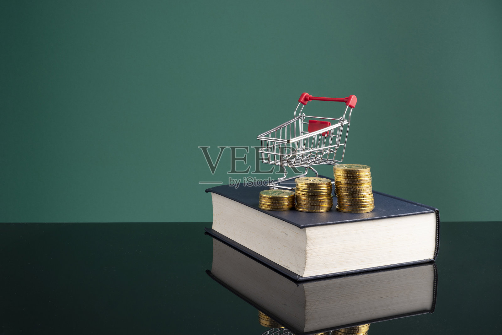 桌子上放着一本书，背景是绿色的，近距离拍摄的储蓄罐、购物车和堆叠的硬币。照片摄影图片