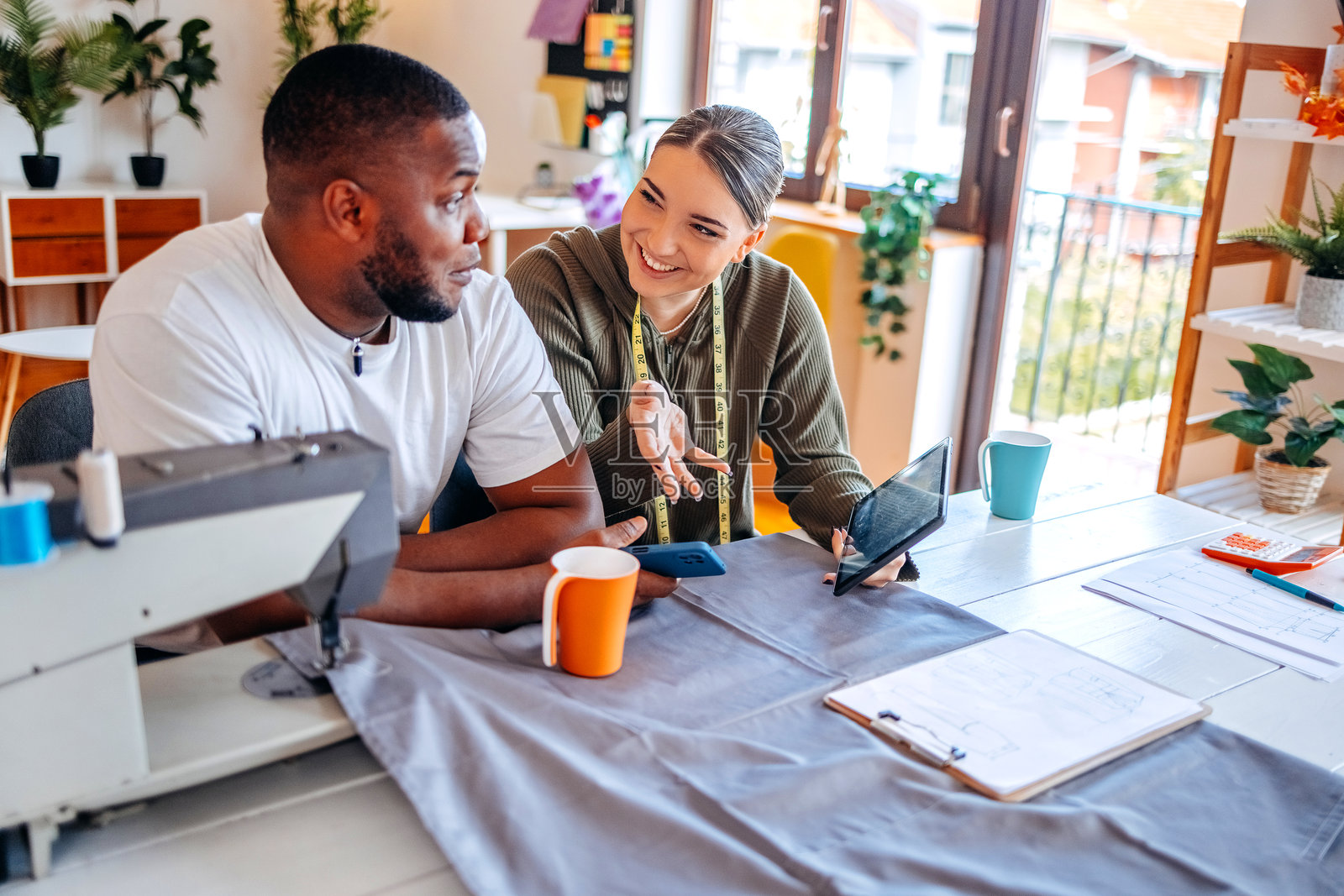 人们在家里用缝纫机修理衣物，但目前正在休息喝咖啡，同时在展示数字平板上的内容。照片摄影图片