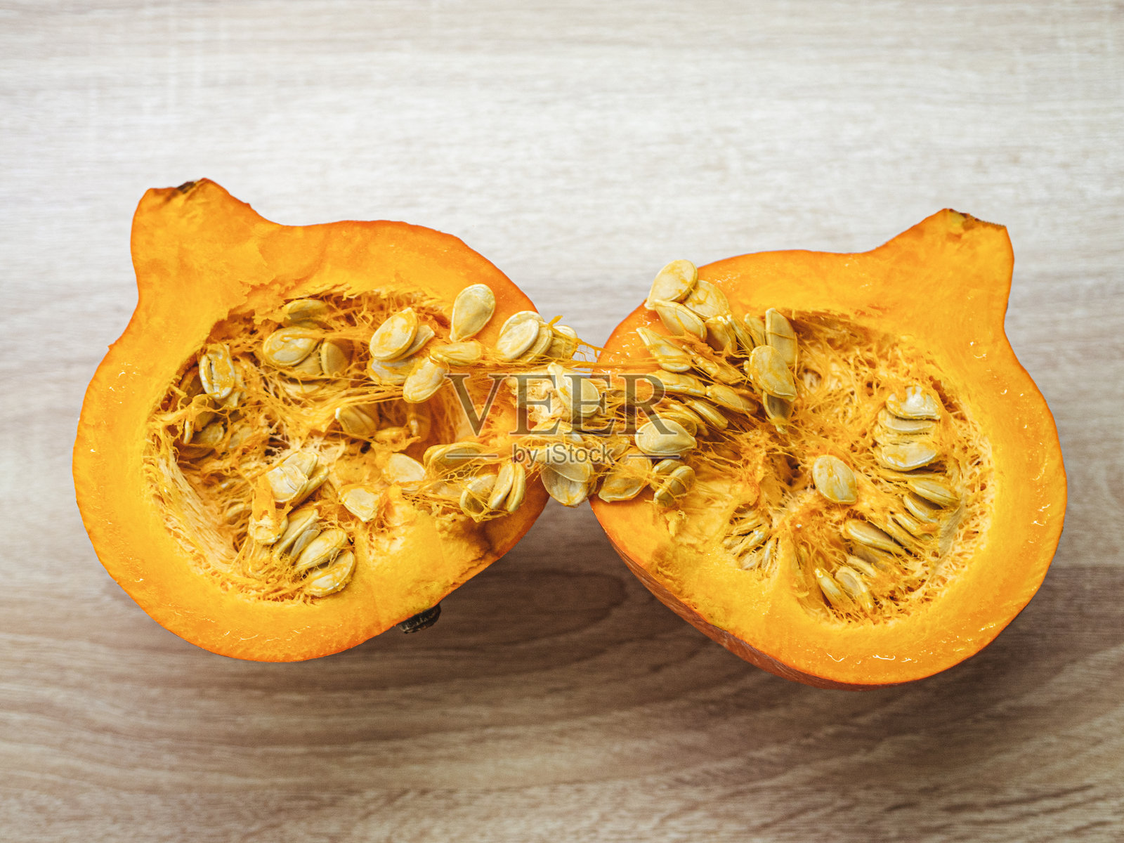 切成两半的橙色北海道南瓜，带有种子，放在木桌上照片摄影图片