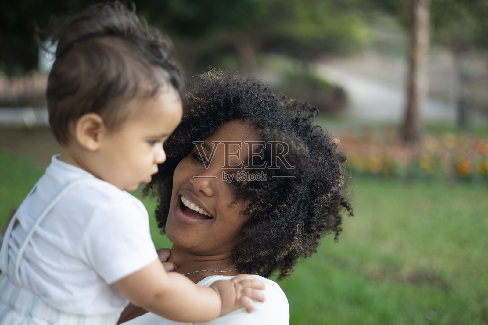 母亲在公园里高兴地抱着她的男婴微笑照片摄影图片