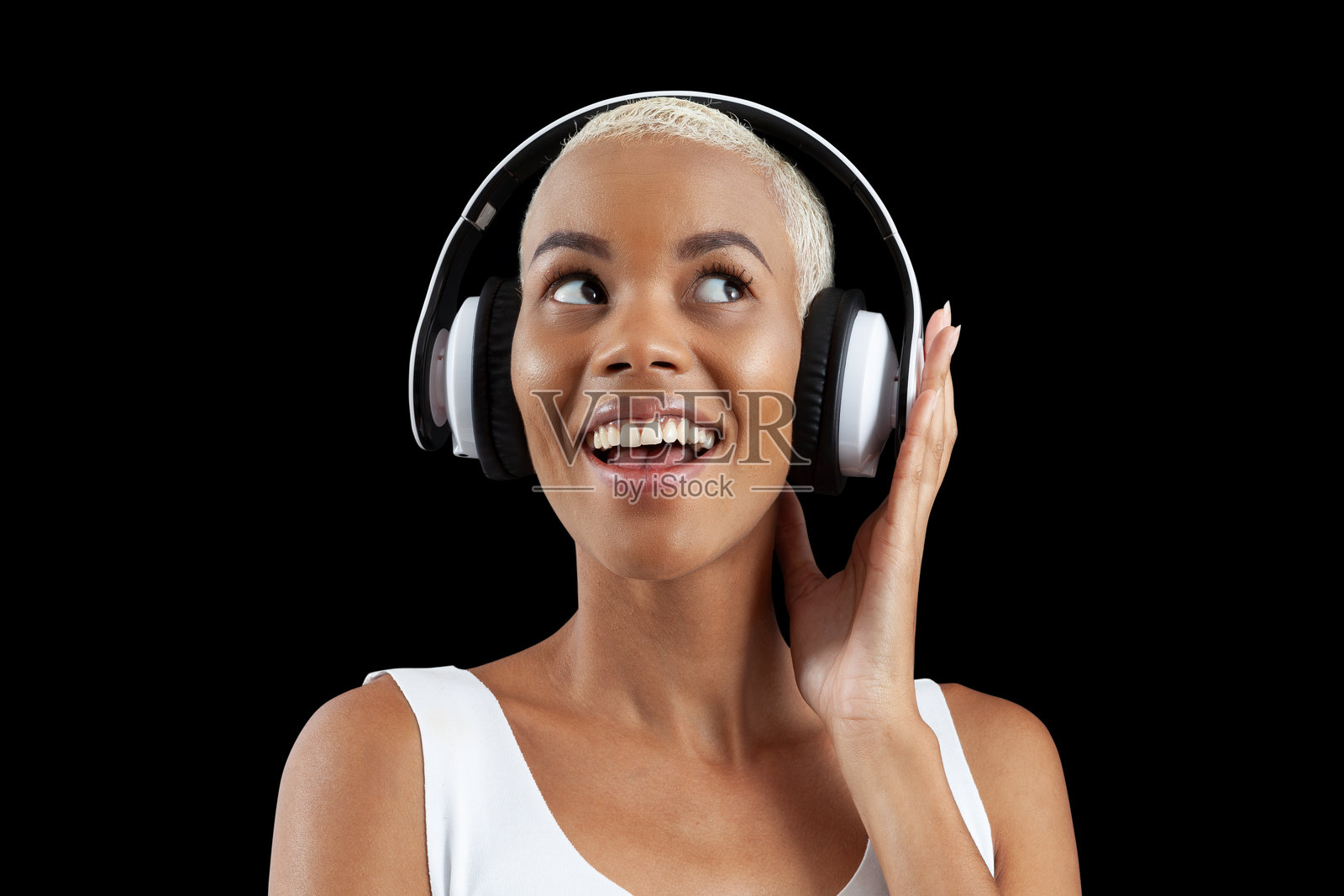 微笑的非洲女性佩戴白色耳机，听着音乐播放列表或播客，侧脸笑容，背景为黑色。照片摄影图片