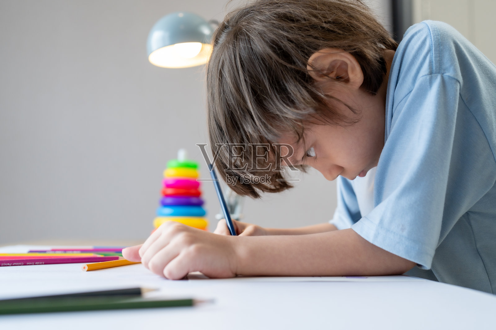 男孩用彩色铅笔在桌子上专心绘画照片摄影图片