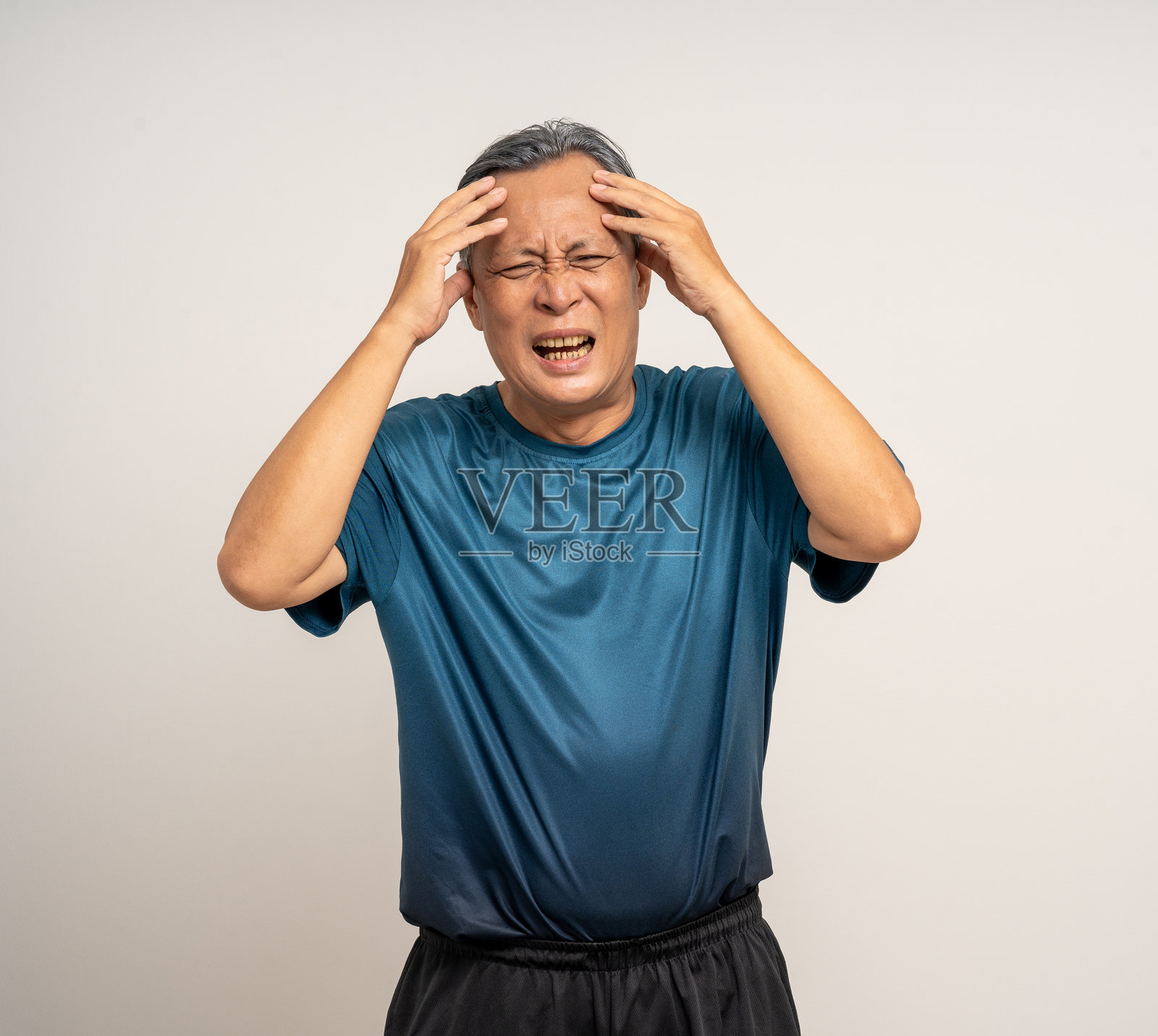 头痛的亚洲老人穿着运动服站在白色背景前。照片摄影图片