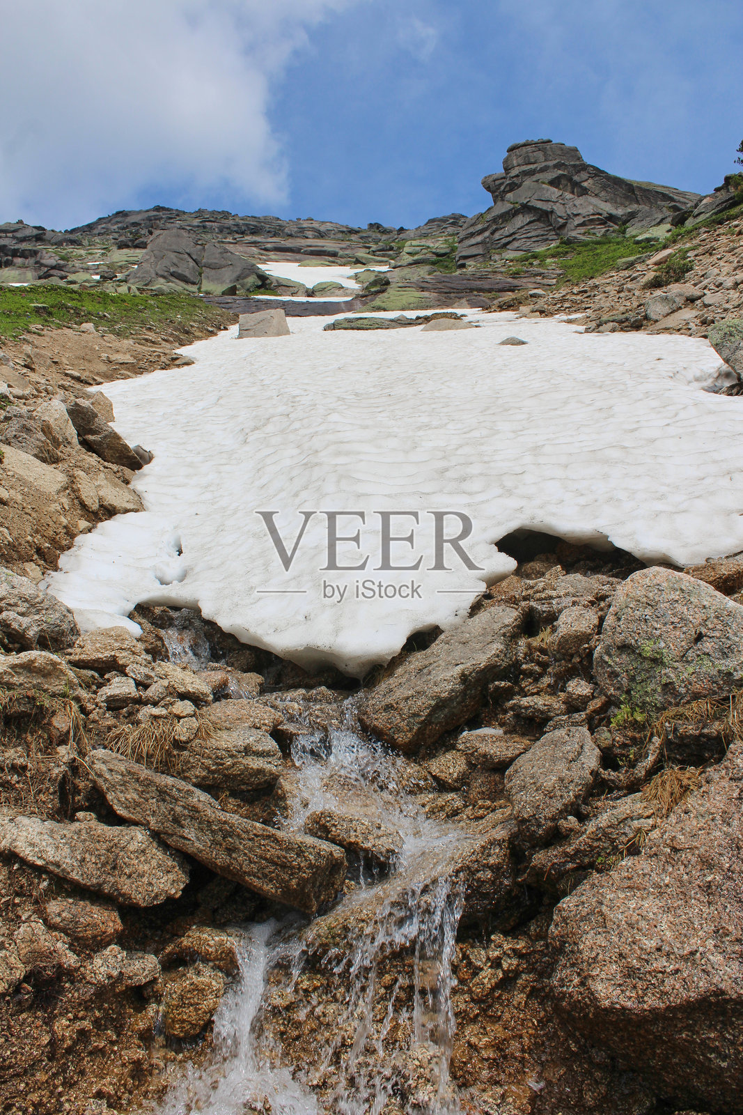 一条溪流在石头之间流淌，从山上的一堆雪中流出。照片摄影图片