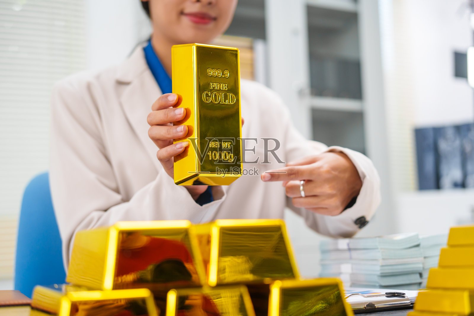 一位亚洲女商人坐在办公桌前，与投资者讨论金条、存款和黄金市场，她分析了黄金价格趋势，强调了投资黄金的长期利益照片摄影图片