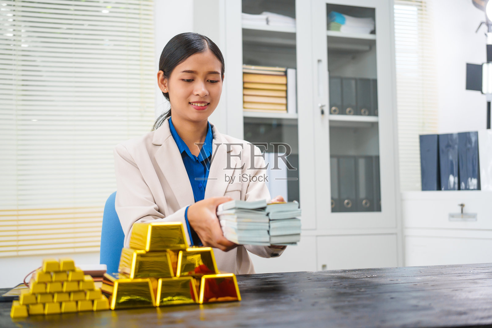 一位亚洲女商人在她的办公桌前坐着，与投资者讨论金条、存款和黄金市场。她分析黄金价格趋势，强调投资黄金的长期收益。照片摄影图片