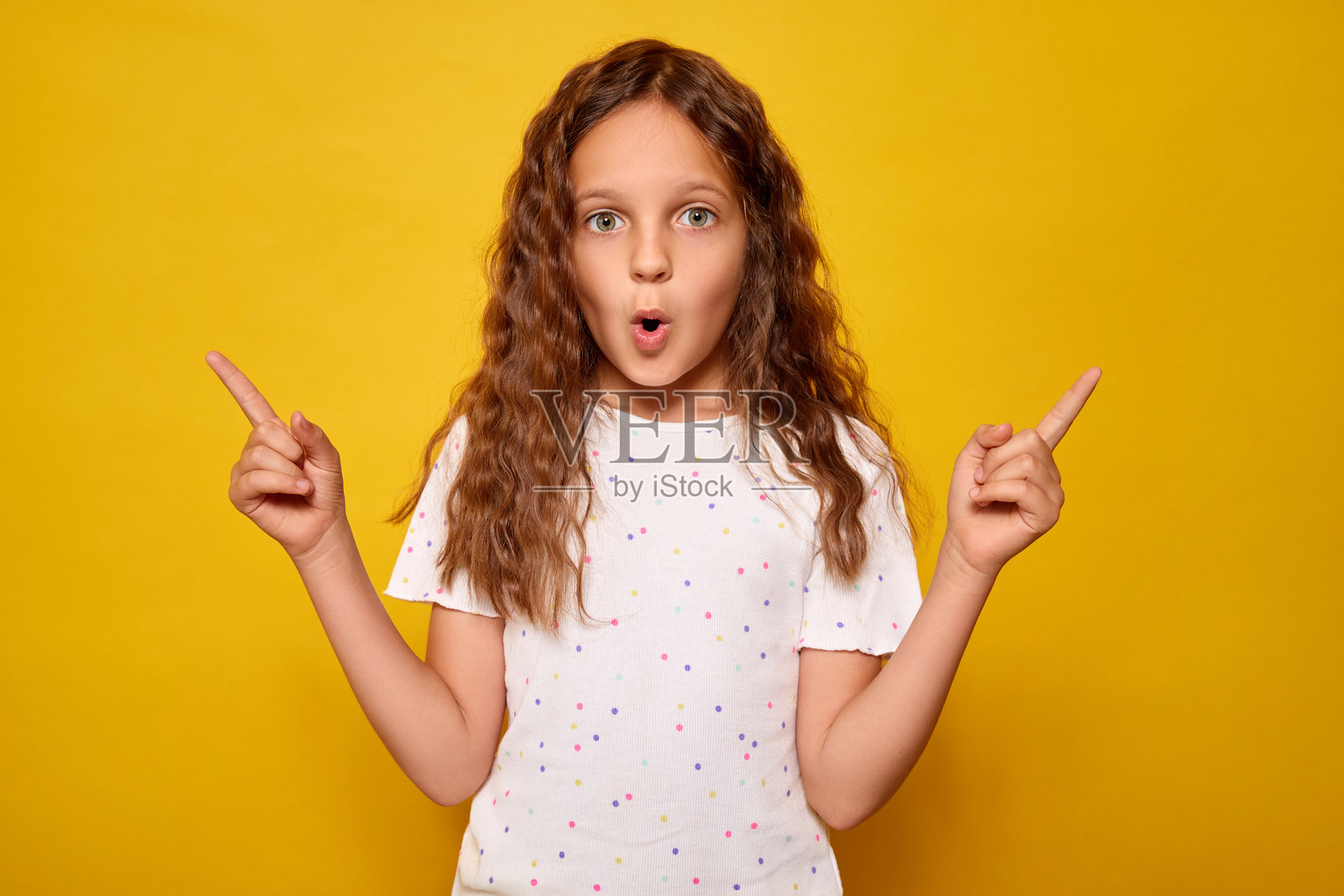震惊的小女孩站在鲜艳的黄色背景前，兴奋地举起手臂，指向两侧的广告位照片摄影图片
