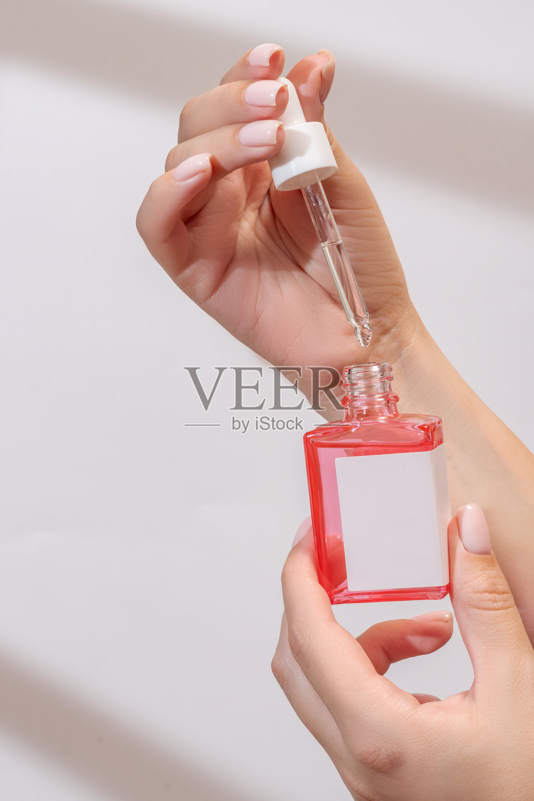 女性手持滴管，滴入精油、香薰精华、美容精华或药用液体，背景为浅色。无品牌瓶子供您设计使用。照片摄影图片