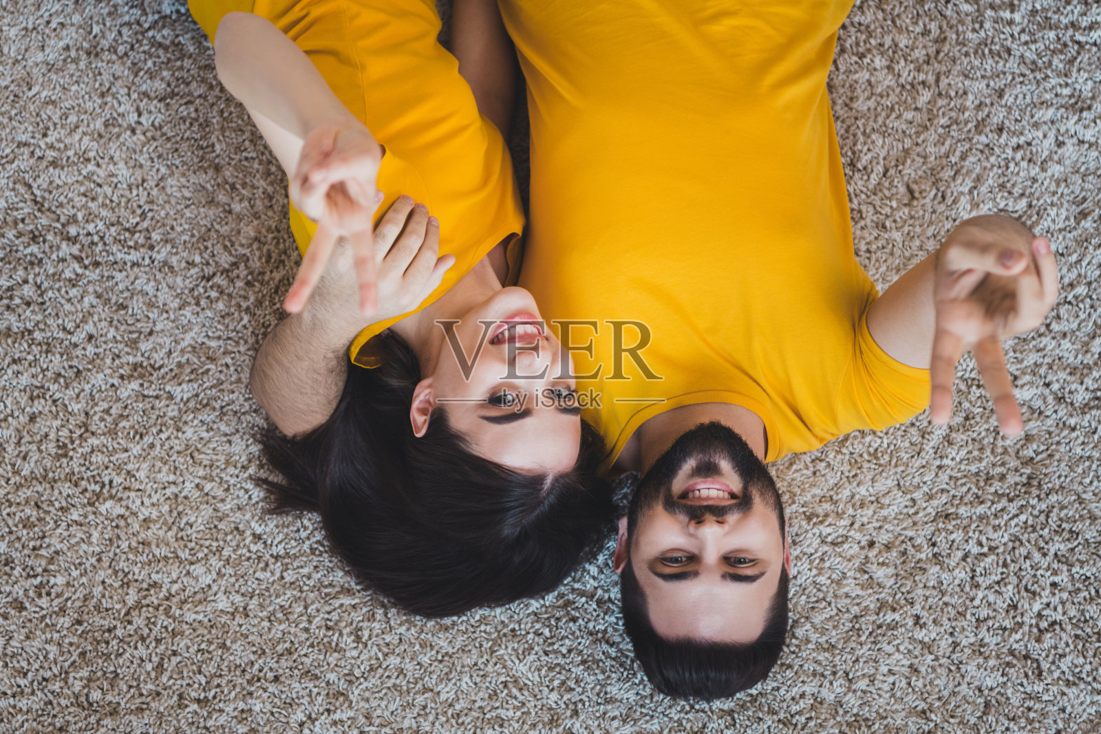俯拍：现代公寓内年轻搭档倒躺地毯比V手势照片摄影图片