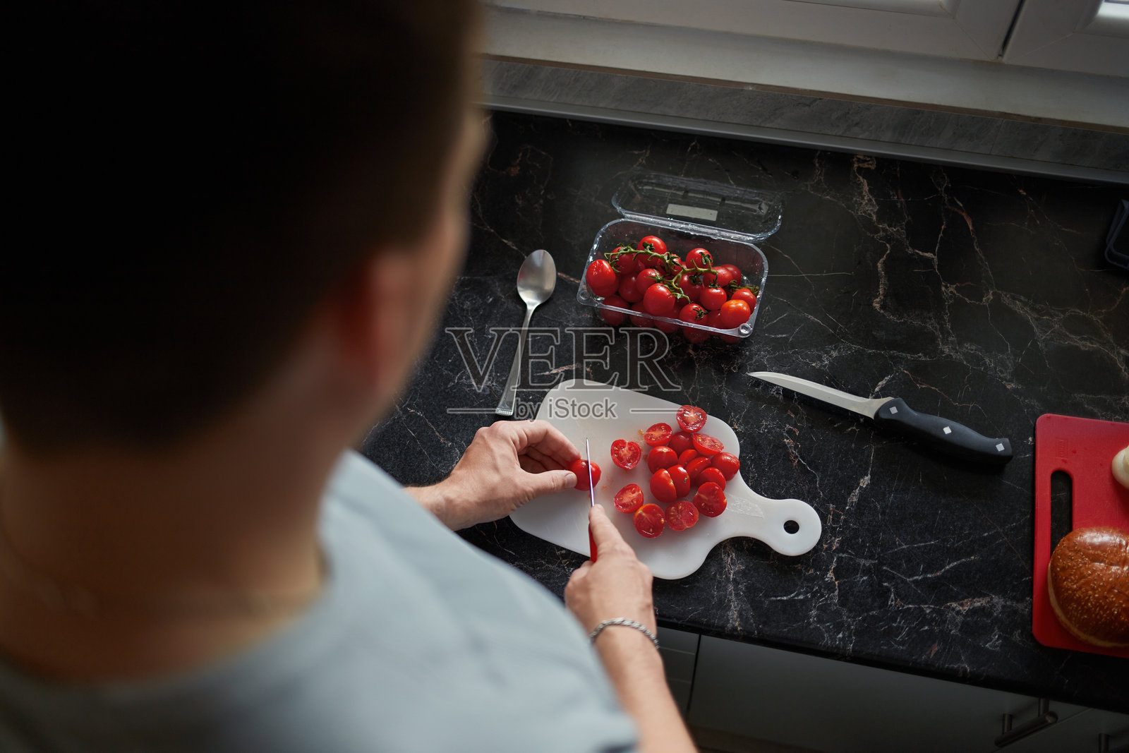 年轻男人在家里的厨房切圣女果，俯视角度照片摄影图片