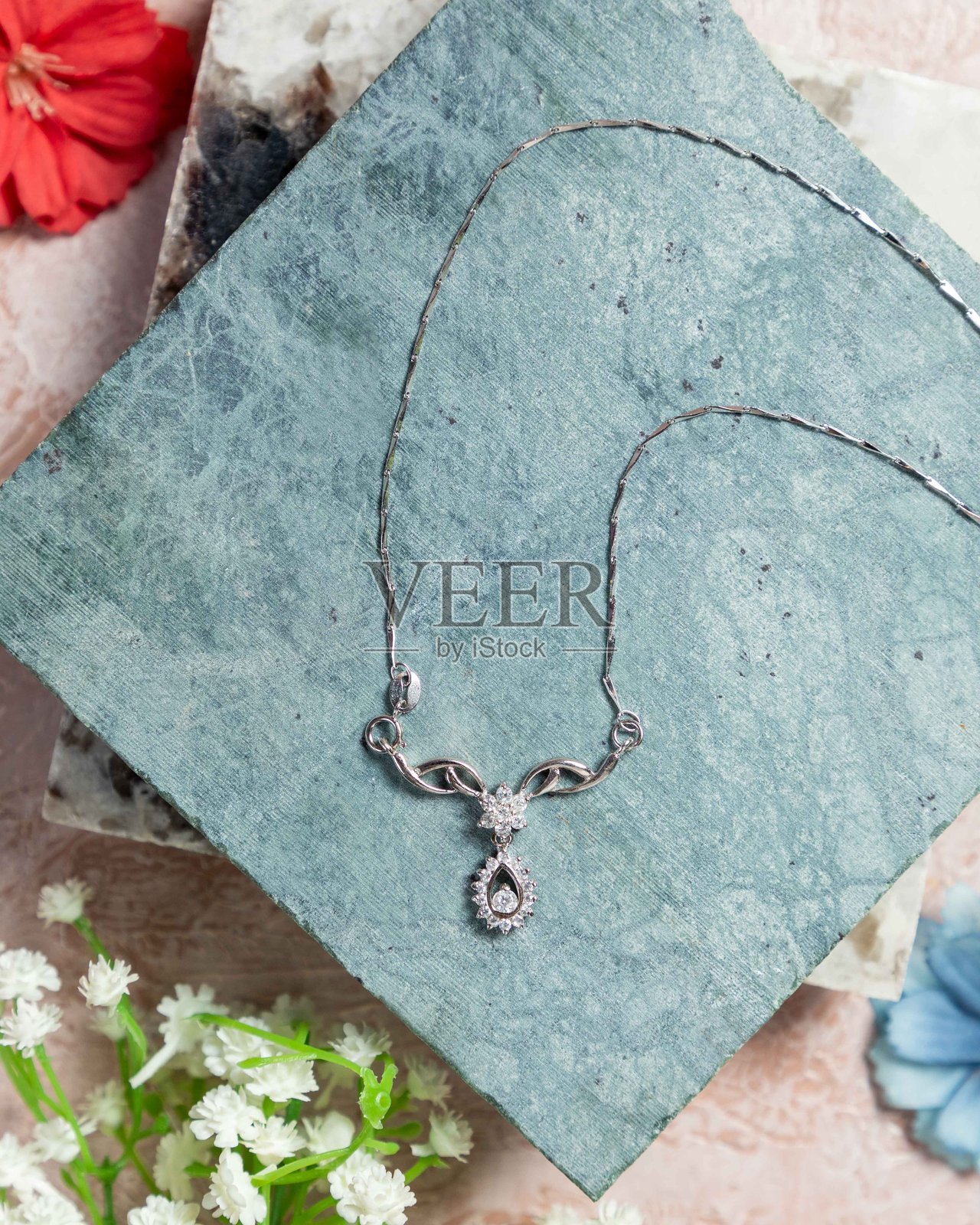 银色项链上镶嵌着钻石，静静地放在蓝色石头和花朵上。照片摄影图片