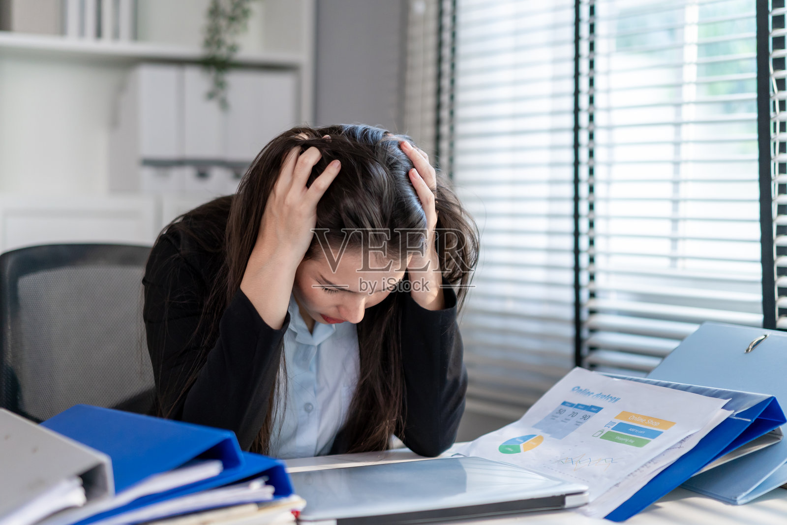 沮丧的混血女商人因工作过度在办公室里工作到很晚。有吸引力的忙碌员工坐在办公桌前，在处理许多纸质文件时感到压力和失望。照片摄影图片