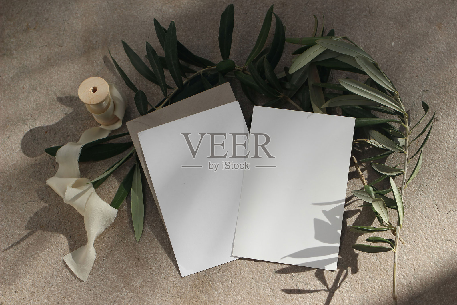 地中海夏季婚礼文具。生日样机。空白贺卡和信封的组合。粗糙的石灰石地板背景。丝带。阳光下的橄榄树枝。平铺，俯视。照片摄影图片