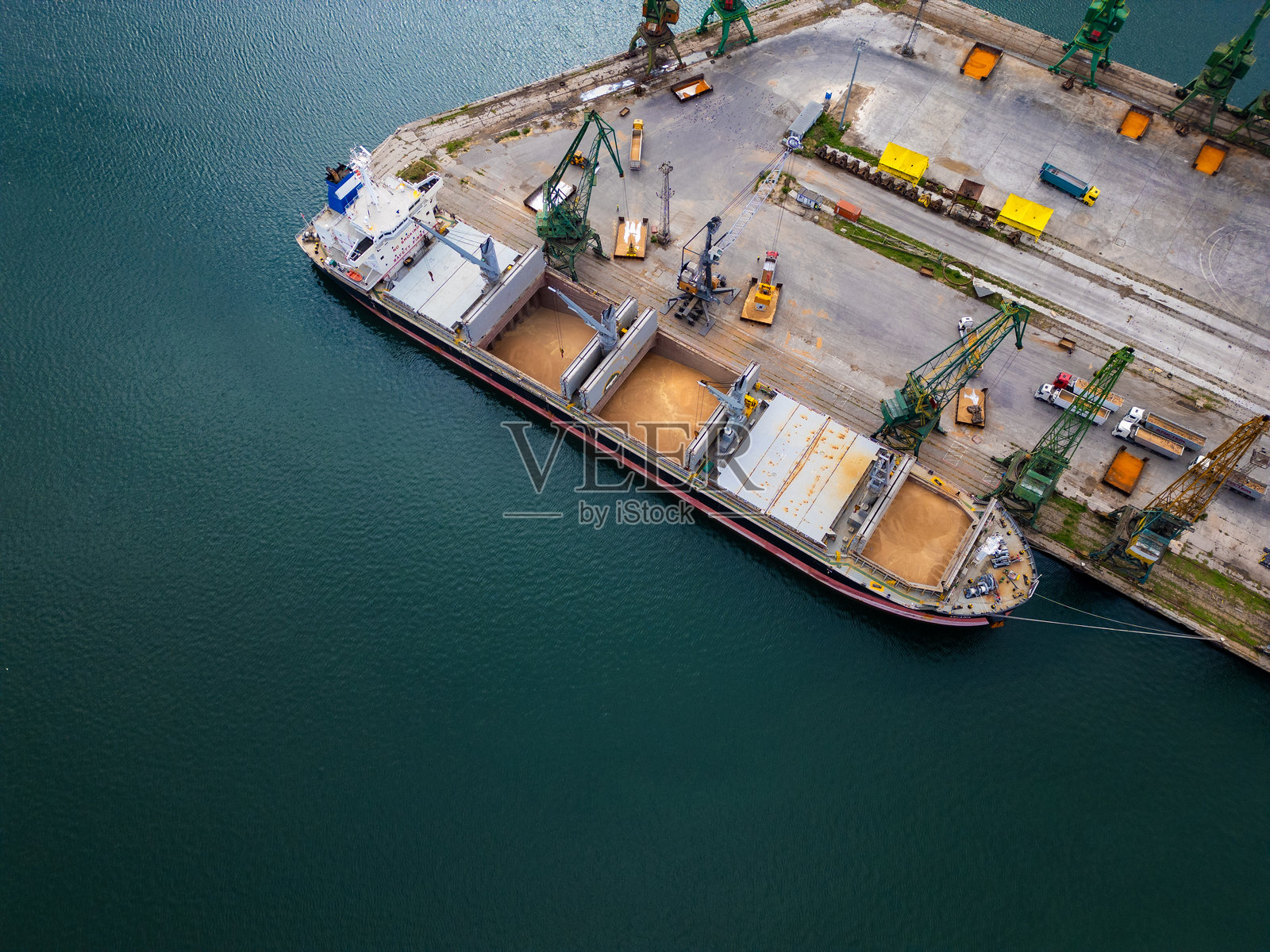 白天时分，繁忙港口中一艘货船在码头装卸谷物的鸟瞰图照片摄影图片