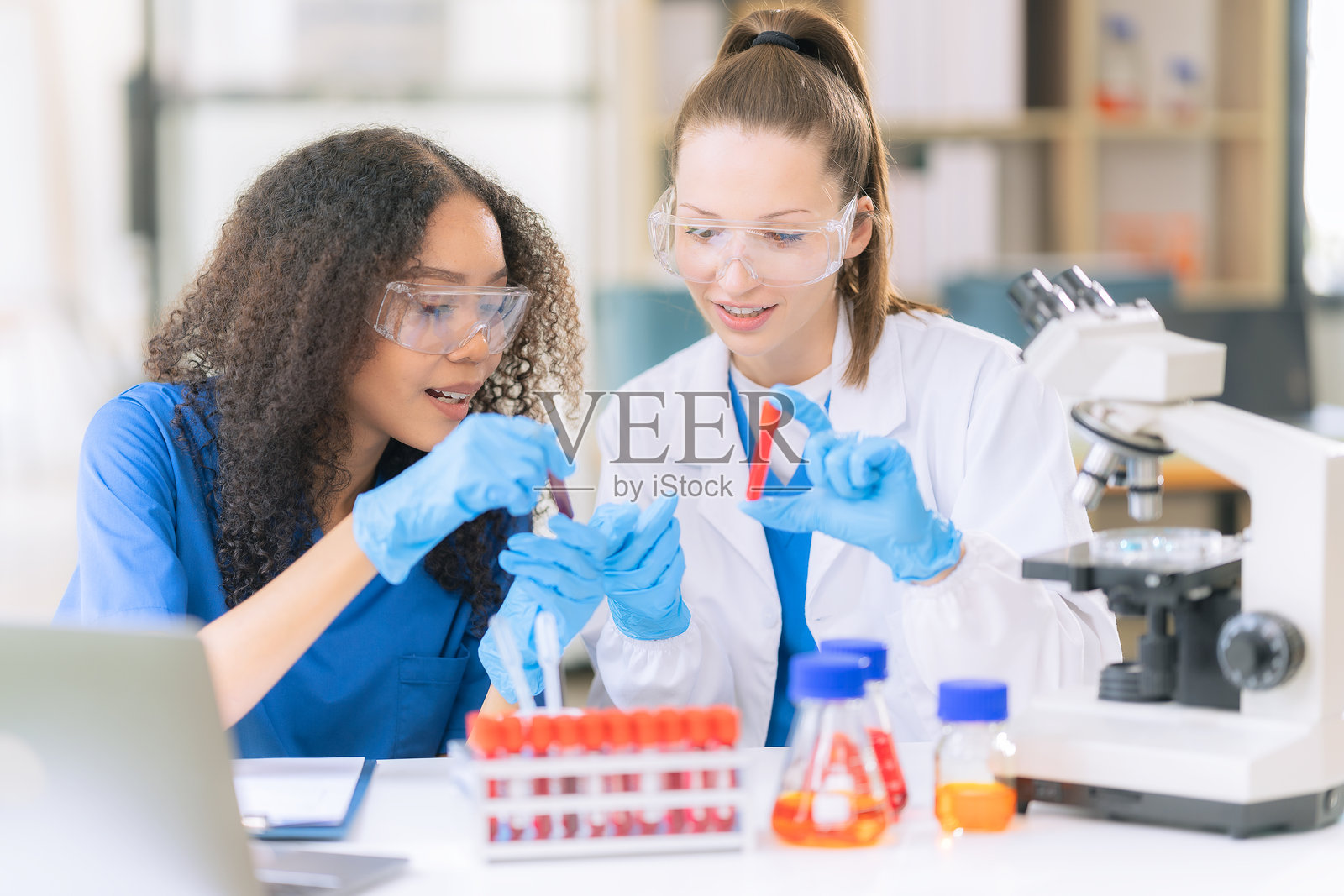 两位女科学家在实验室工作，用滴管从试管中吸取血液样本和溶液，进行研究照片摄影图片
