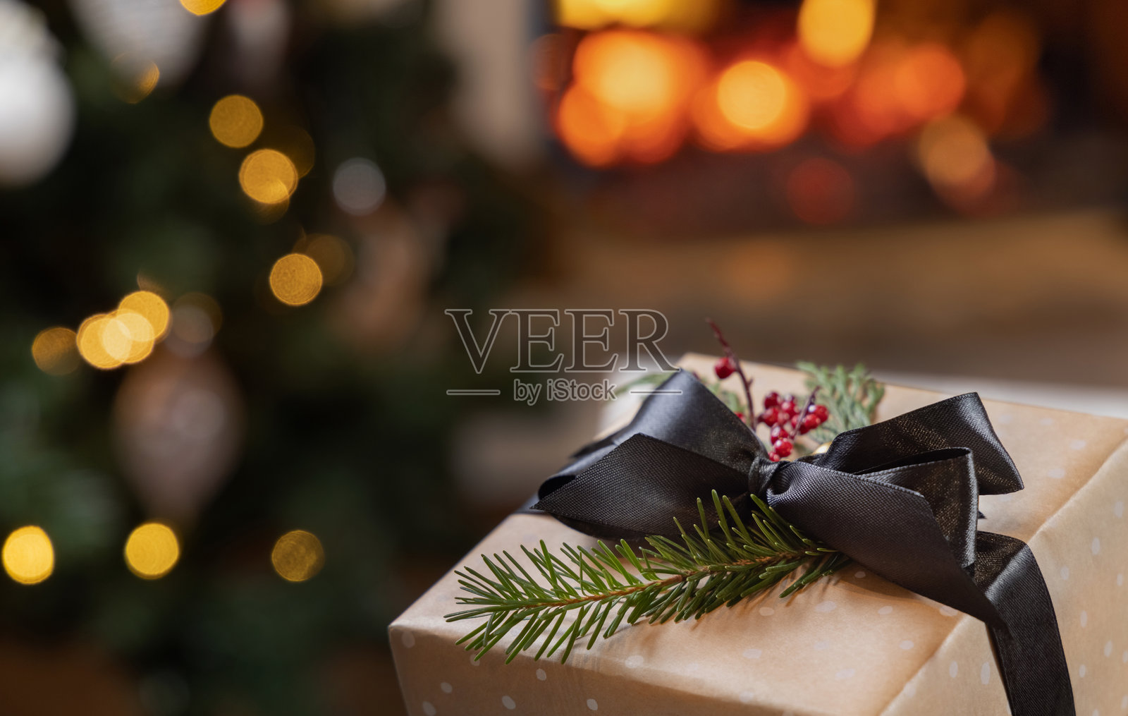 燃烧的壁炉和圣诞树灯光下的黑色蝴蝶结圣诞礼物照片摄影图片