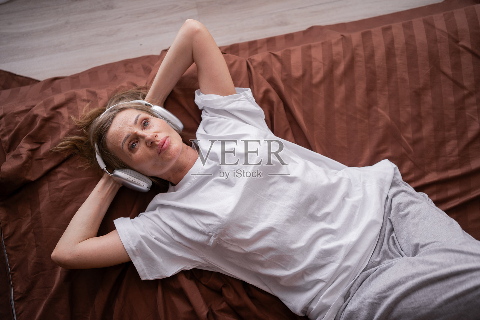 中年女性躺在床上，戴着耳机，享受音乐，放松身心，度过一个宁静的周末。照片摄影图片