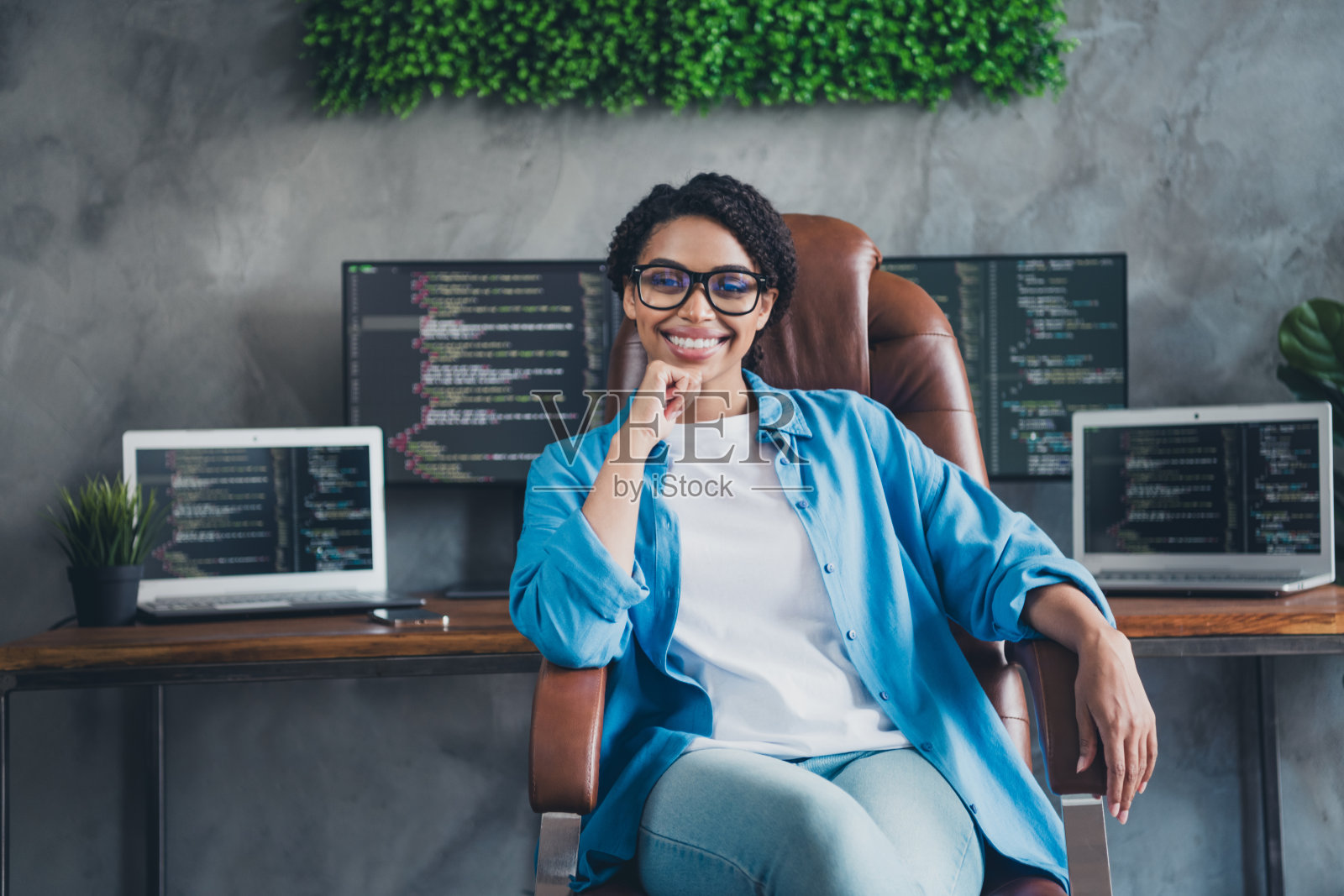 年轻女孩坐在扶手椅上，自信微笑，蓝色衬衫，程序员办公室照片摄影图片