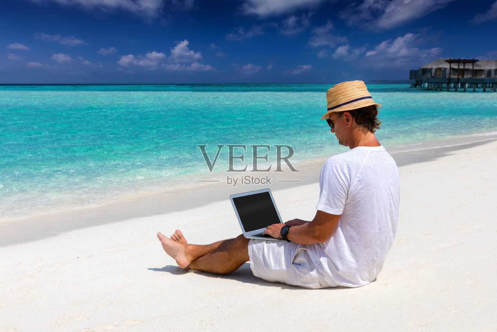 阳光明媚的日子里，男人在海滩上使用笔记本电脑。照片摄影图片