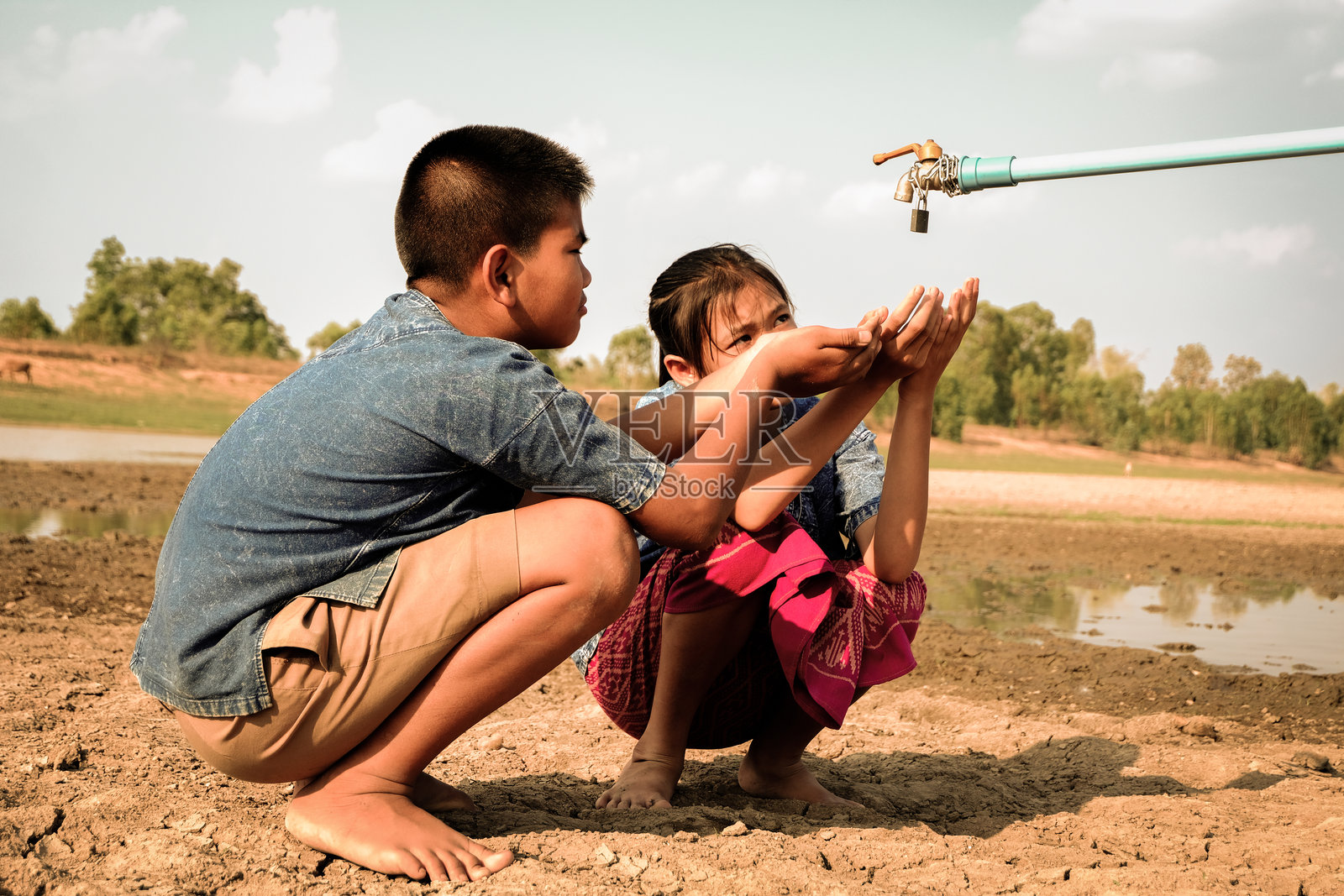 贫瘠土地上水龙头旁蹲着的儿童全身照片摄影图片