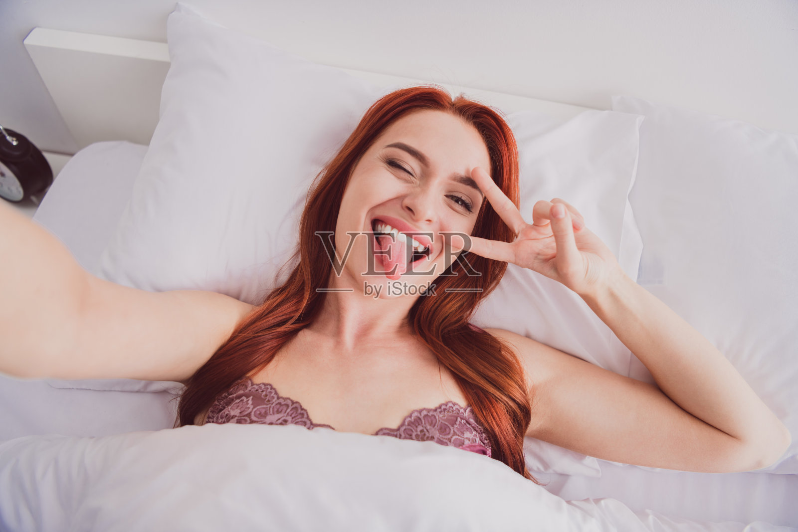 快乐可爱的女孩博主在室内白色灯光下自拍录制视频，做出V字手势。照片摄影图片