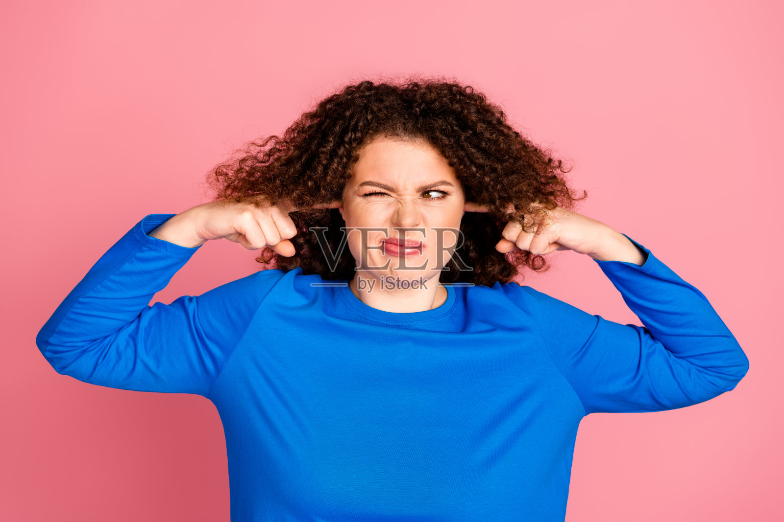 年轻的红发女性，卷发，穿着蓝色毛衣，在粉色背景前表达沮丧。照片摄影图片