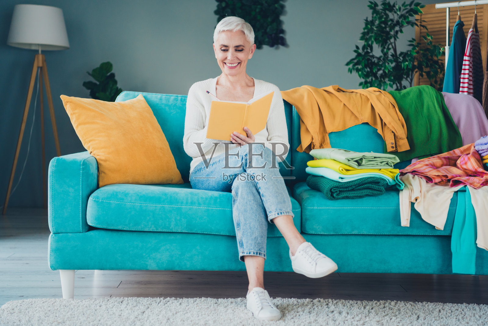 可爱的迷人女性穿着白色开衫，在室内杂乱的房间里阅读清洁任务计划。照片摄影图片