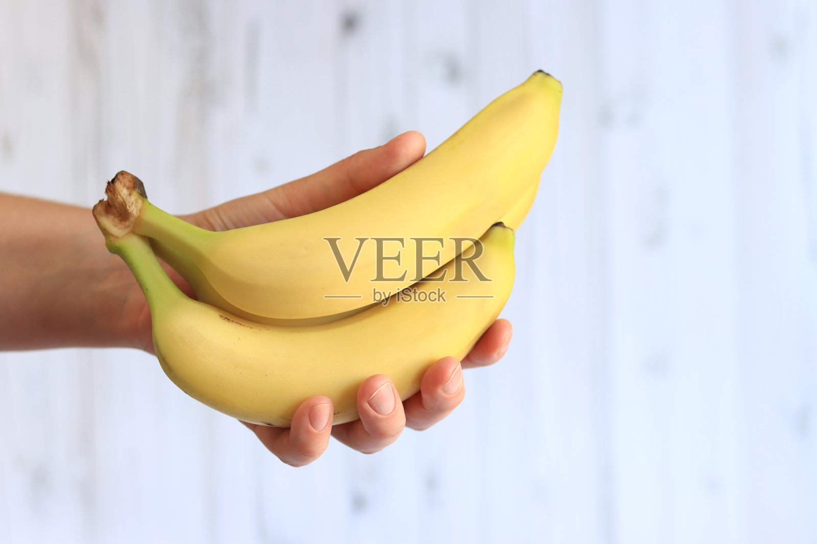 女人手中拿着香蕉，背景为浅色。照片摄影图片