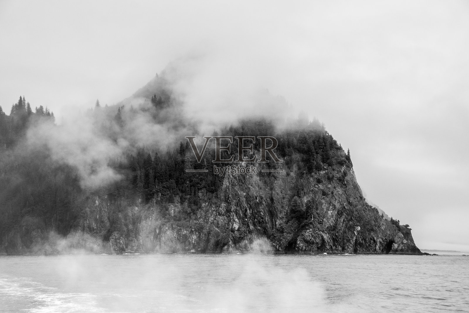 一张黑白照片，展示了肯奈峡湾国家公园的岛屿和岩石 formations，拍摄于低云和雾气弥漫的日子。照片摄影图片