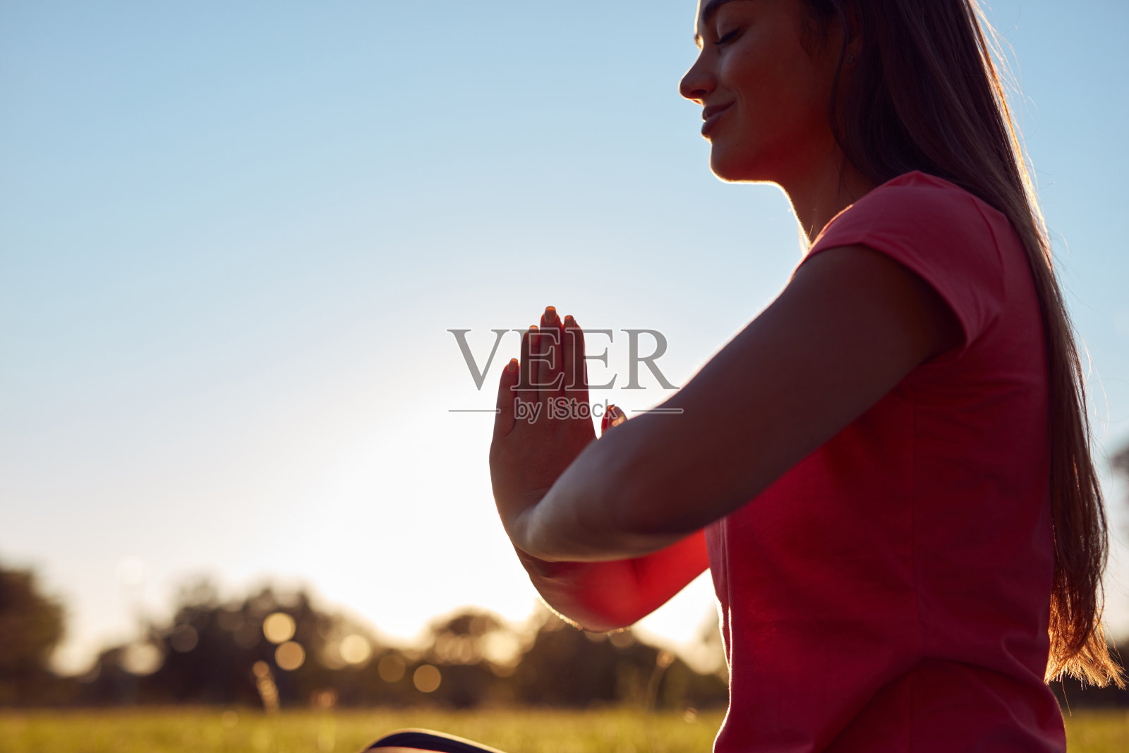 年轻女性在公园的草地上，夏季日落时分在运动瑜伽垫上锻炼。照片摄影图片