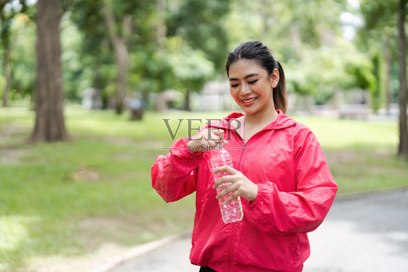 晴朗的一天，在公园里打开水瓶的红衣女子照片摄影图片