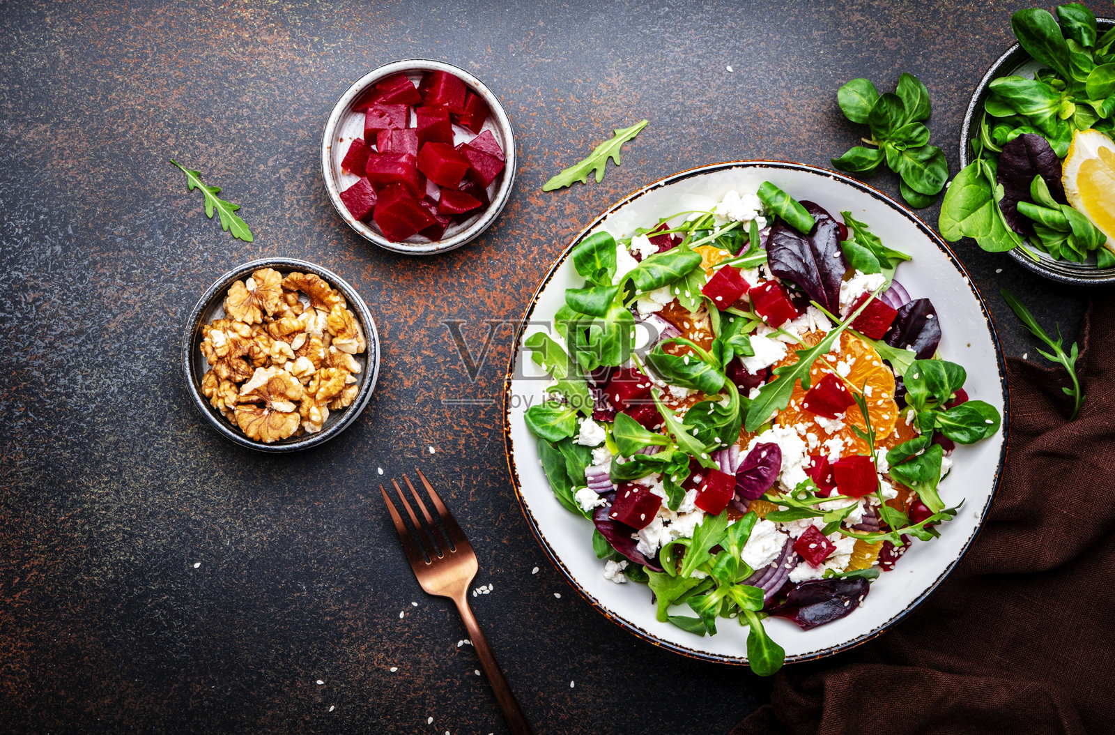 美食爱好者的沙拉，配有甜菜根、瑞可塔奶酪和橘子，搭配生菜和洋葱。棕色背景。俯视图。照片摄影图片